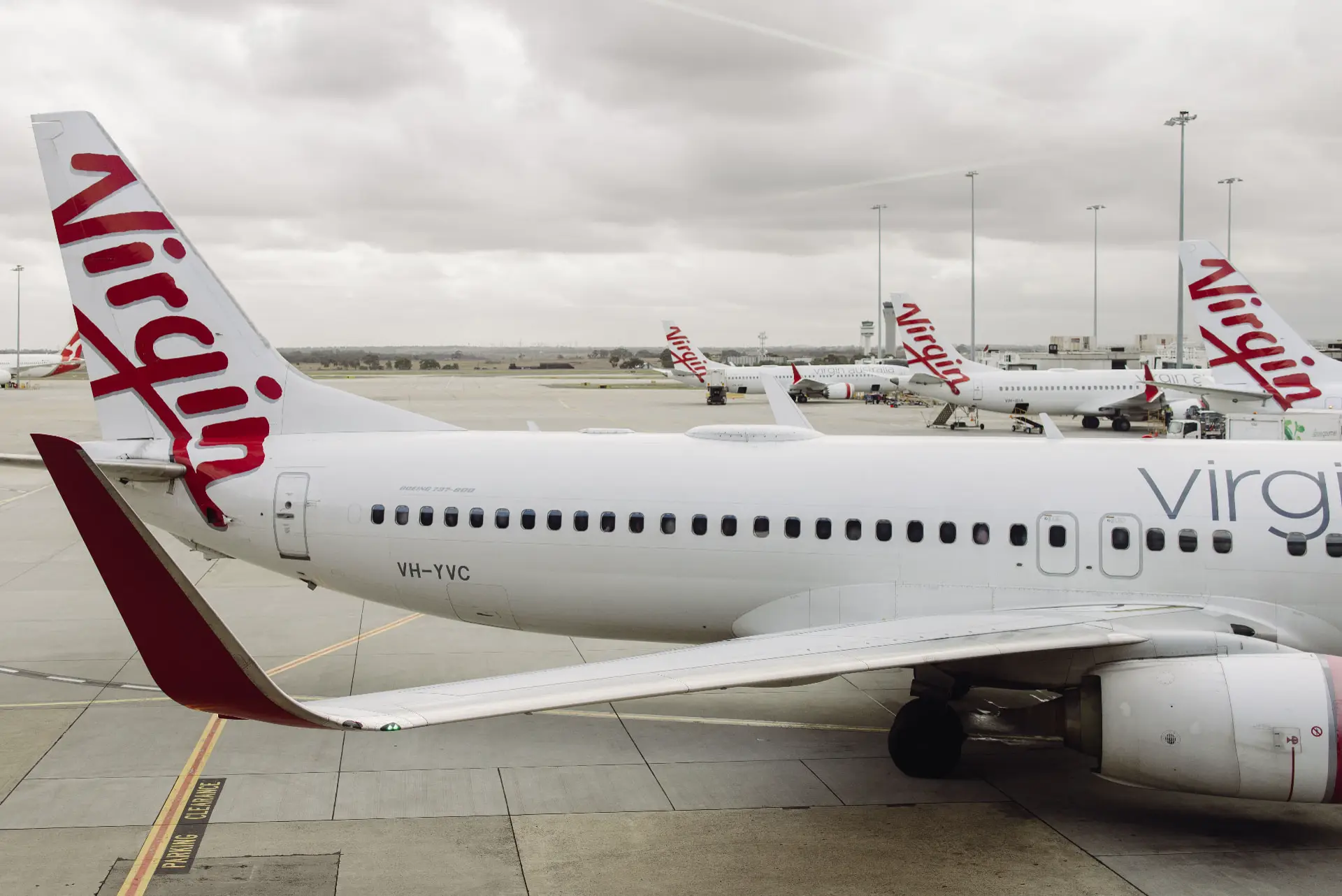 Virgin Australia Boeing 737 parked on the apron with the wider fleet and ground handling crews behind it